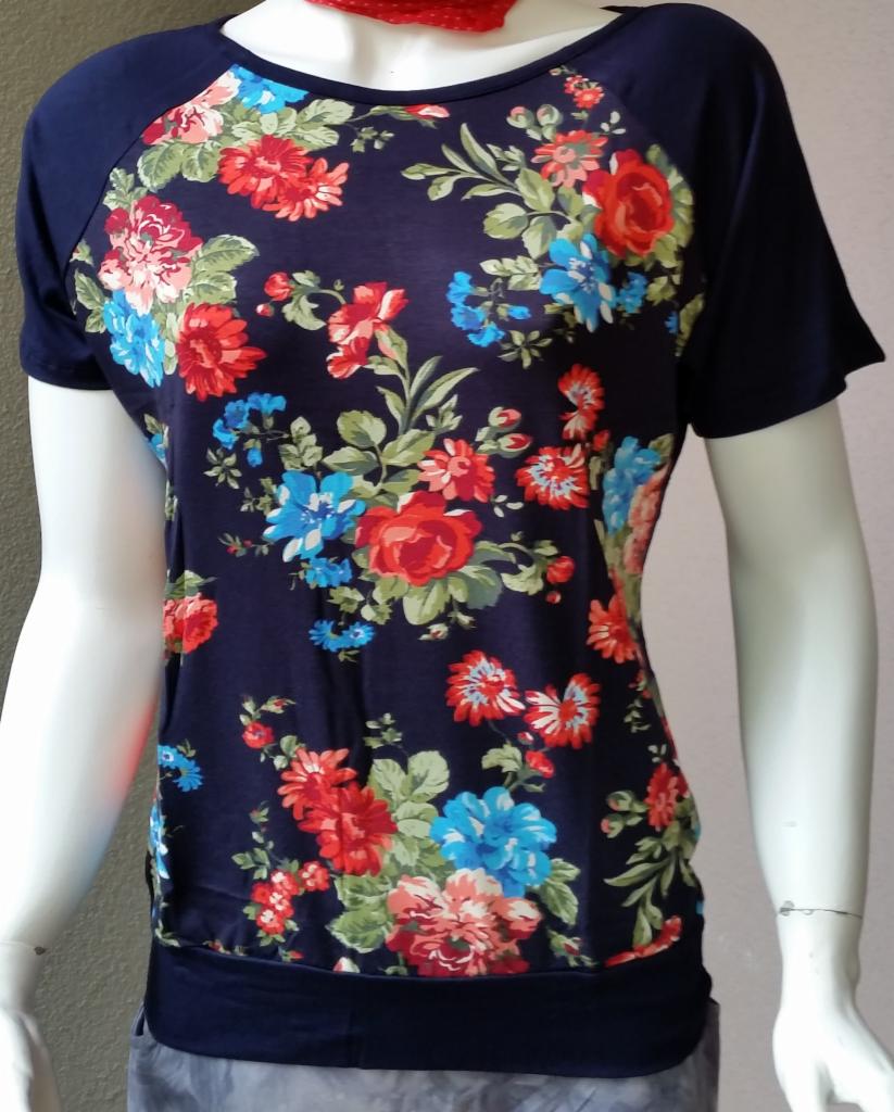 Granatowa bluzka damska z krótkim rękawem, pokryta wzorem z czerwonych i niebieskich kwiatów, prezentowana na manekinie z czerwoną apaszką.