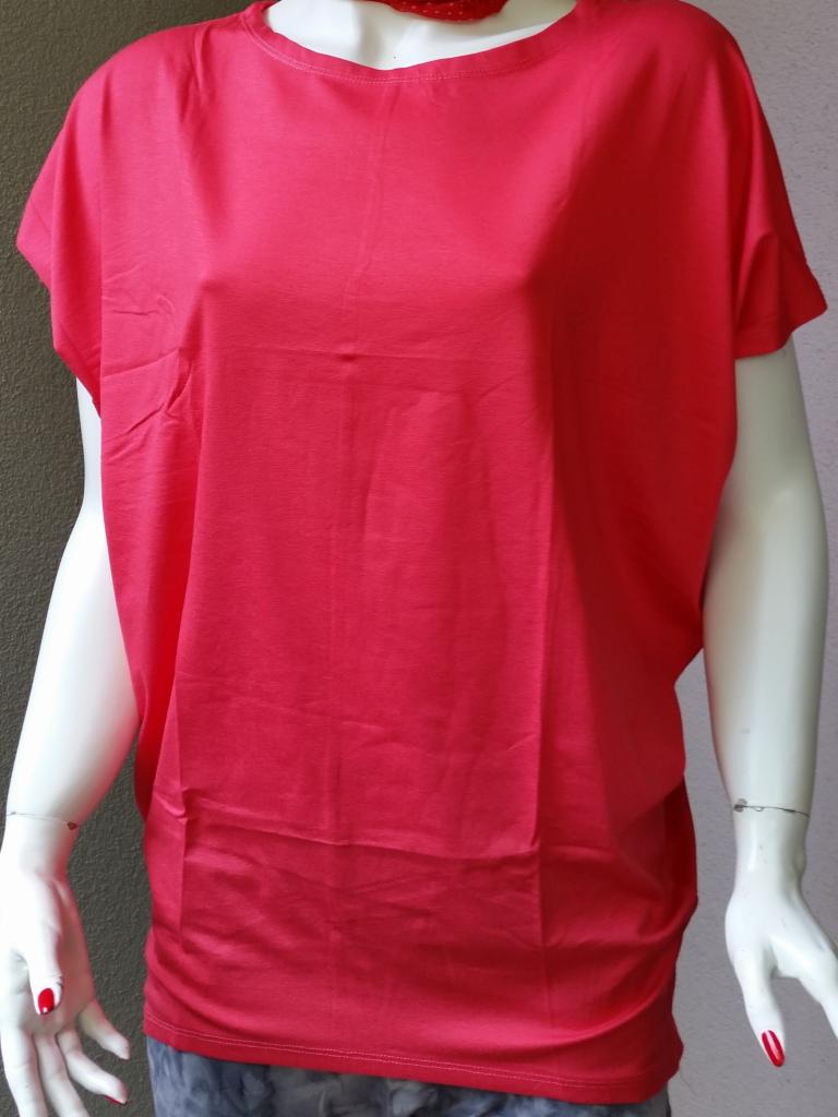 Czerwona bluzka damska z krótkim rękawem, prezentowana na manekinie z widocznym naszyjnikiem w kropki i delikatną bransoletką. Stonowane tło.