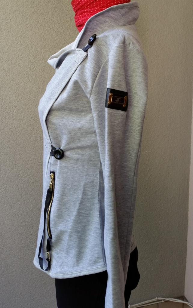 Szara, rozpinana bluza damska z asymetrycznym zapięciem, widoczna z boku, z czarnymi detalami: zamek, guzik i naszywka z logo na rękawie. Czerwona apaszka w tle.