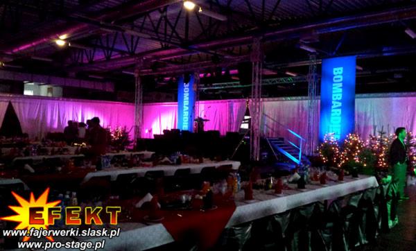 Sala bankietowa z oświetleniem eventowym w odcieniach różu i fioletu, sceną z podestem, dekoracjami świątecznymi i banerami reklamowymi.