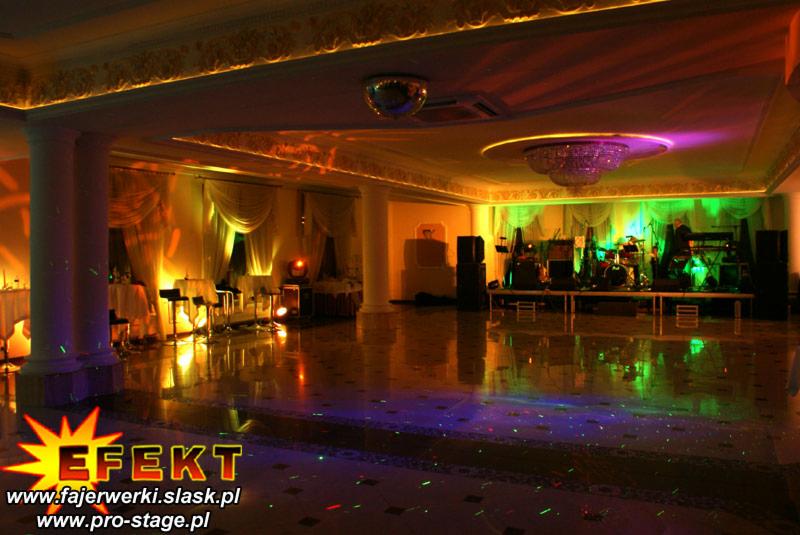 Sala bankietowa z oświetleniem eventowym: reflektory, lustrzana kula, scena z zespołem. Podłoga odbija światła, tworząc efektowną grę barw.