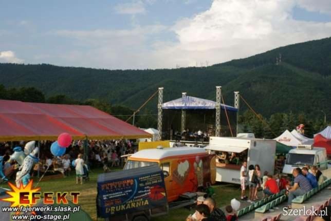 Plenerowa impreza z widokiem na góry: scena, namioty cateringowe, food trucki i tłum ludzi. Letni festyn z nagłośnieniem i zapleczem gastronomicznym.