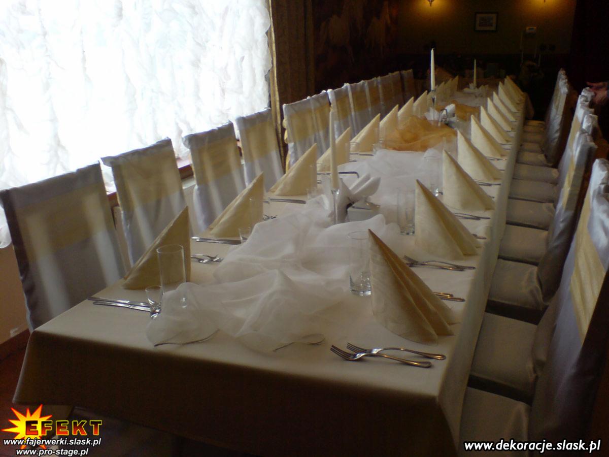 Długi stół z nakryciami i krzesłami udekorowanymi na uroczystość, widok z perspektywy końca stołu, z oknem w tle i delikatnym oświetleniem.