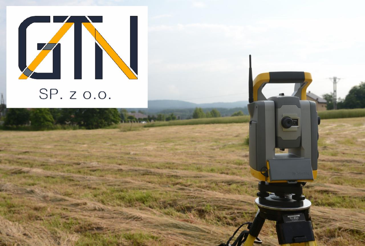 Tachimetr Trimble na trójnogu na polu ze skoszoną trawą, logo firmy GTN SP. z o.o. w lewym górnym rogu.