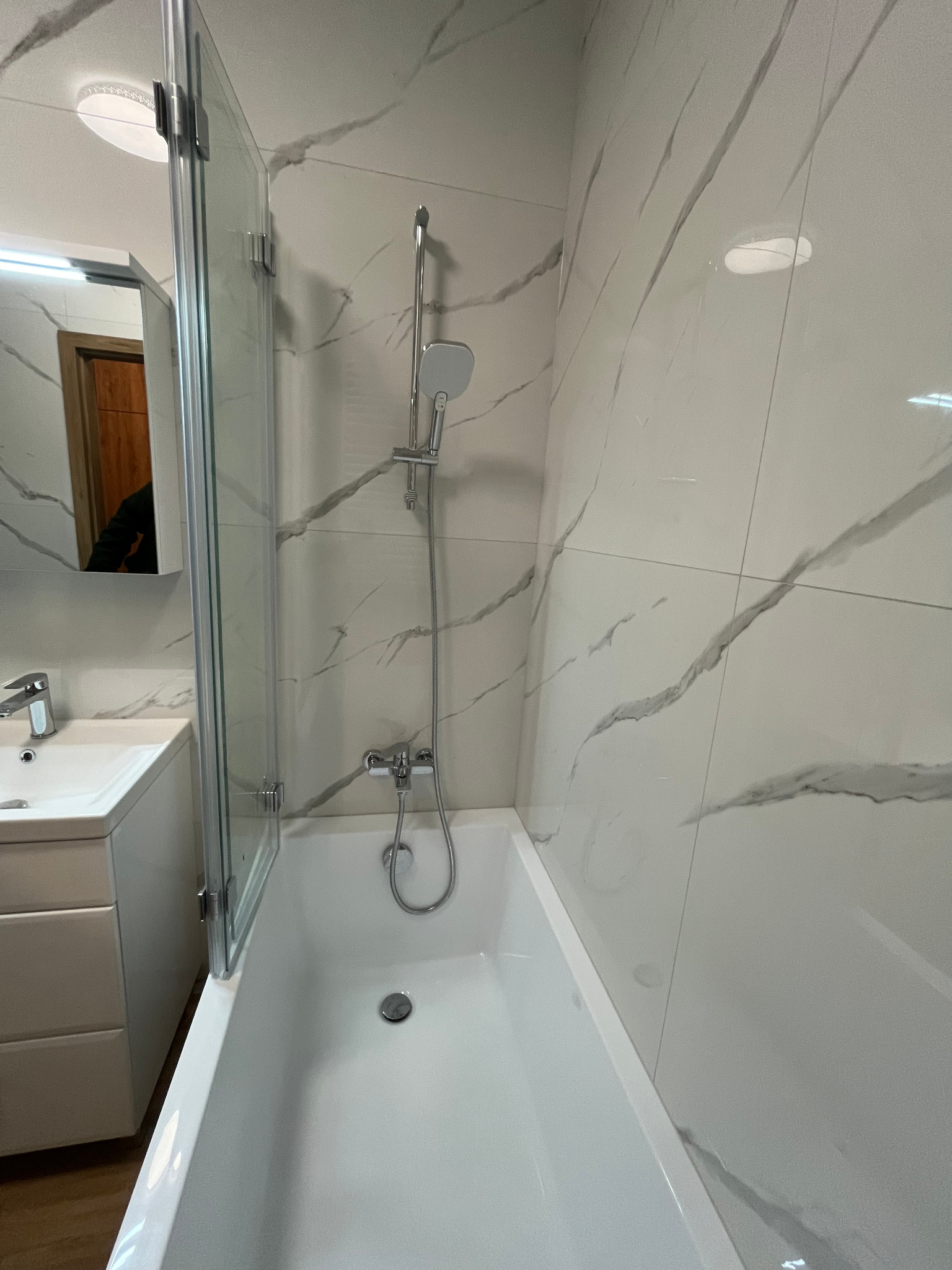 Nowoczesna łazienka w Warszawie z wanną, szklanym parawanem nawannowym i umywalką w zabudowie, wykończona białymi płytkami imitującymi marmur.