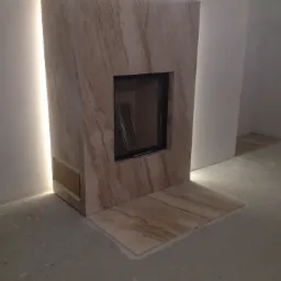 Obudowa kominka z marmuru z podświetleniem LED, widoczne zabezpieczenie otworu wentylacyjnego taśmą malarską, niedokończona podłoga.