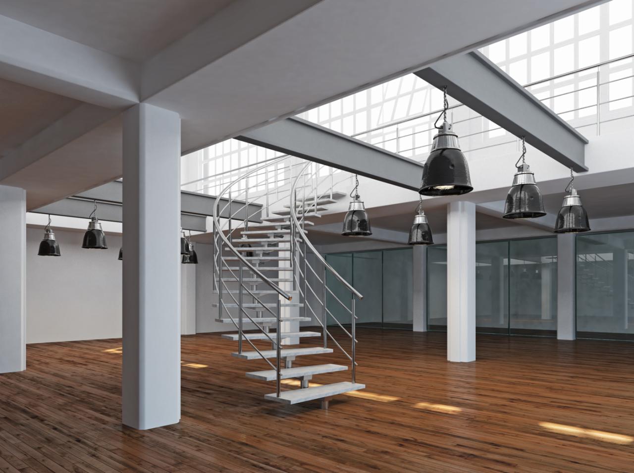 Nowoczesne, spiralne schody metalowe z drewnianymi stopniami w przestronnym, loftowym wnętrzu z dużymi oknami i industrialnym oświetleniem.