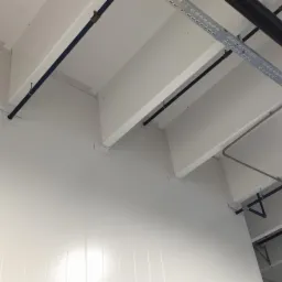 Wnętrze hali z zamontowanymi białymi płytami warstwowymi na ścianach i suficie. Widoczne rury instalacyjne i elementy konstrukcyjne.