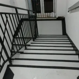 Schody z czarno-białymi stopniami i czarną metalową balustradą, widziane z góry.