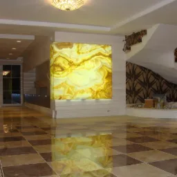 Wnętrze holu z marmurową podłogą w szachownicę i podświetlanym panelem ściennym z onyksu. Schody z dekoracyjną balustradą w tle.