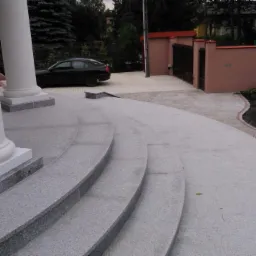 Granitowe schody wejściowe z białymi kolumnami, prowadzące do budynku. W tle widoczny czarny samochód i ogrodzenie posesji.