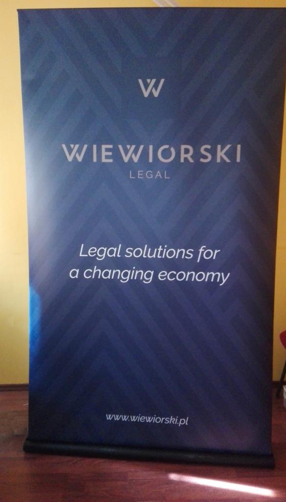 Roll-up reklamowy z logo i nazwą firmy prawniczej Wiewiorski Legal na tle wzoru w jodełkę i hasłem Legal solutions for a changing economy.