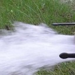 Studnie głębinowe odwierty pompy ciepła woda - Wypływająca woda z metalowej instalacji z zaworami, trawa w tle.