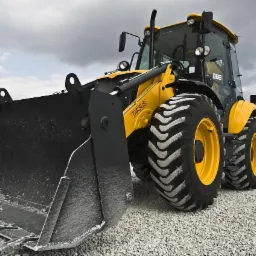 Żółto-czarna ładowarka teleskopowa z pełną łyżką jasnoszarego kruszywa na placu budowy, pochmurne niebo w tle.