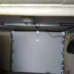 Biała segmentowa brama garażowa z automatyką i sprężynami widoczna od wewnątrz w Gorzowie Wielkopolskim, na ścianie drabina i narzędzia.