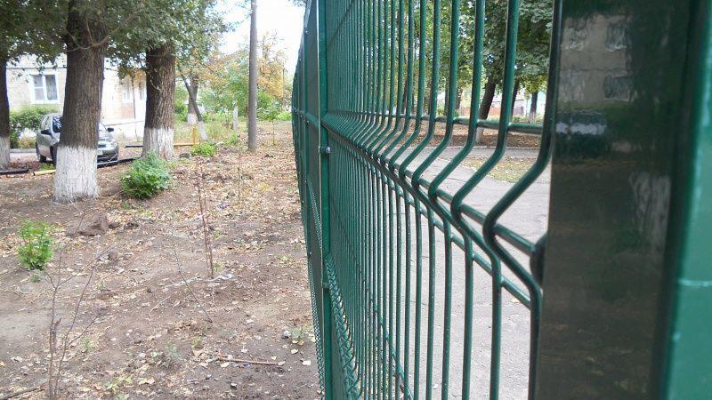 Zielone panele ogrodzeniowe zgrzewane, widok z boku, na tle drzew i budynku.
