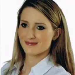 Portret kobiety z długimi blond włosami, ubrana w białą koszulę, uśmiechająca się delikatnie, na jasnym, neutralnym tle.