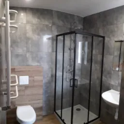 Nowoczesna łazienka z kabiną prysznicową z czarnymi profilami, umywalką nablatową i dużymi szarymi płytkami imitującymi beton.