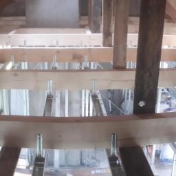 MK Firma Usługowa Michał Kohnke - Konstrukcja poddasza z drewnianych belek i metalowych profili, przygotowana pod montaż izolacji i wykończenie, widok z dołu na drewniany szkielet dachu.