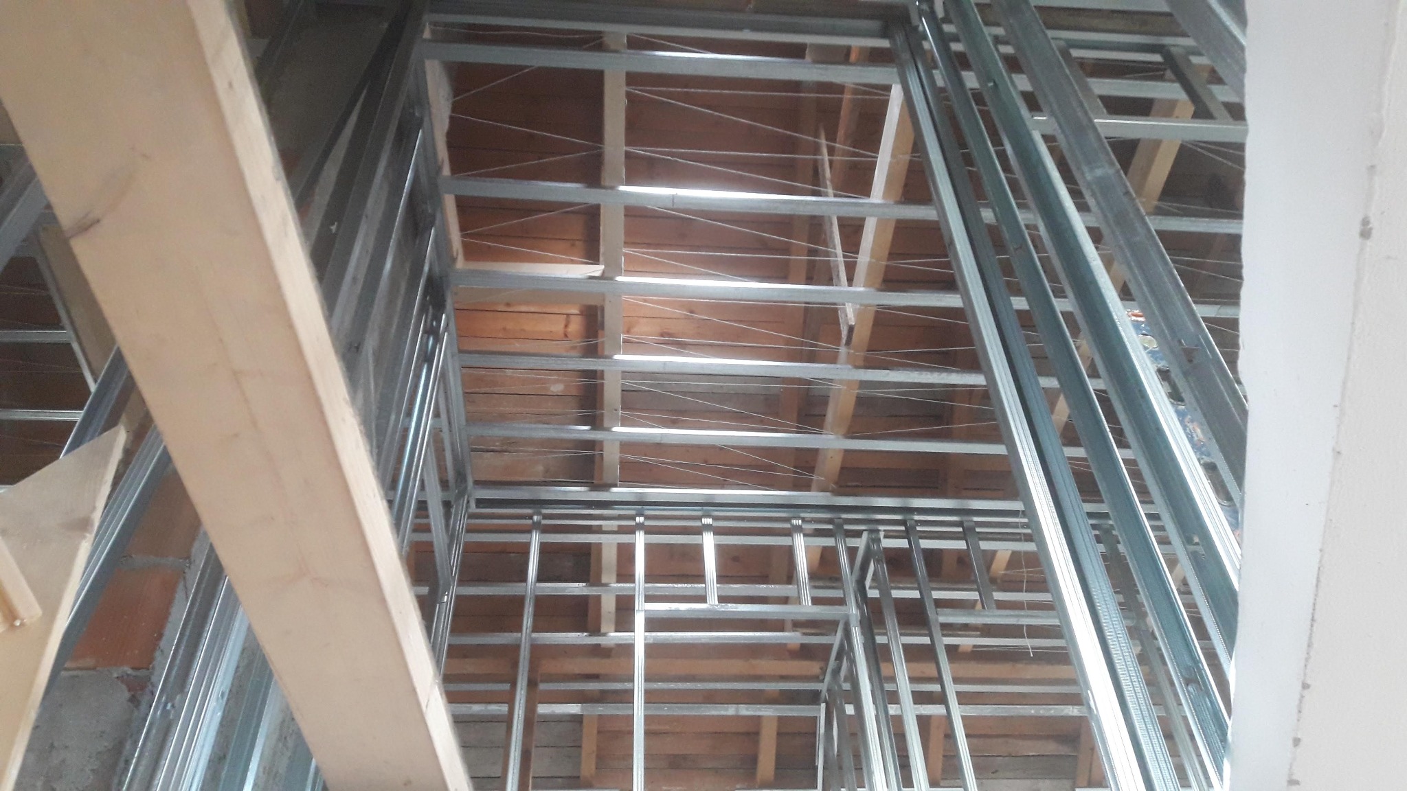 Konstrukcja metalowa z profili pod zabudowę z płyt gipsowo-kartonowych, widoczna drewniana więźba dachowa, surowy stan, przygotowanie do dalszych prac wykończeniowych.