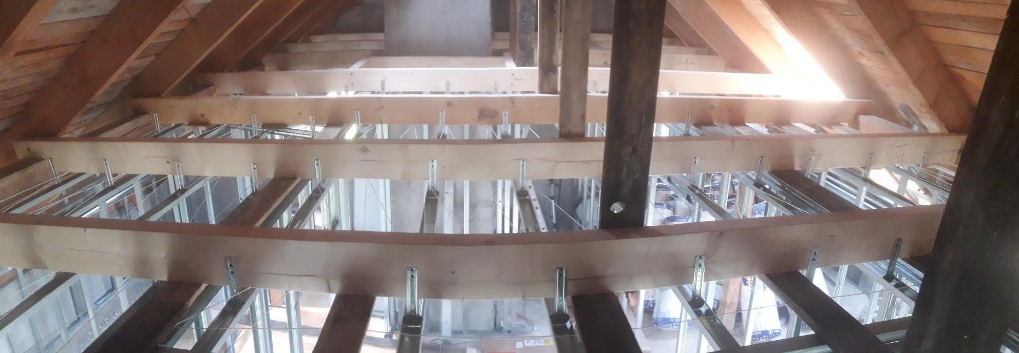 Konstrukcja poddasza z drewnianych belek i metalowych profili, przygotowana pod montaż izolacji i wykończenie, widok z dołu na drewniany szkielet dachu.