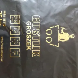 Czarne opakowanie z nadrukiem 'GUSTLIK GROSZEK', informacjami o parametrach opału (kaloryczność, granulacja, popiół, siarka) oraz logotypem przedstawiającym górnika z kilofem.