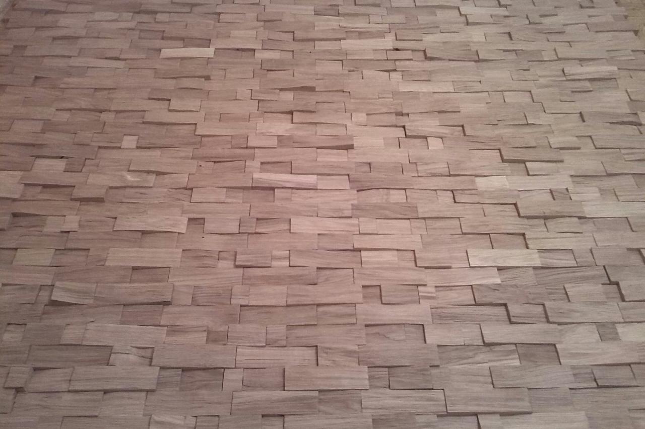 Dekoracyjna okładzina ścienna z drewnianych elementów o nieregularnym kształcie, ułożonych warstwowo. Naturalna kolorystyka drewna, widoczne usłojenie.