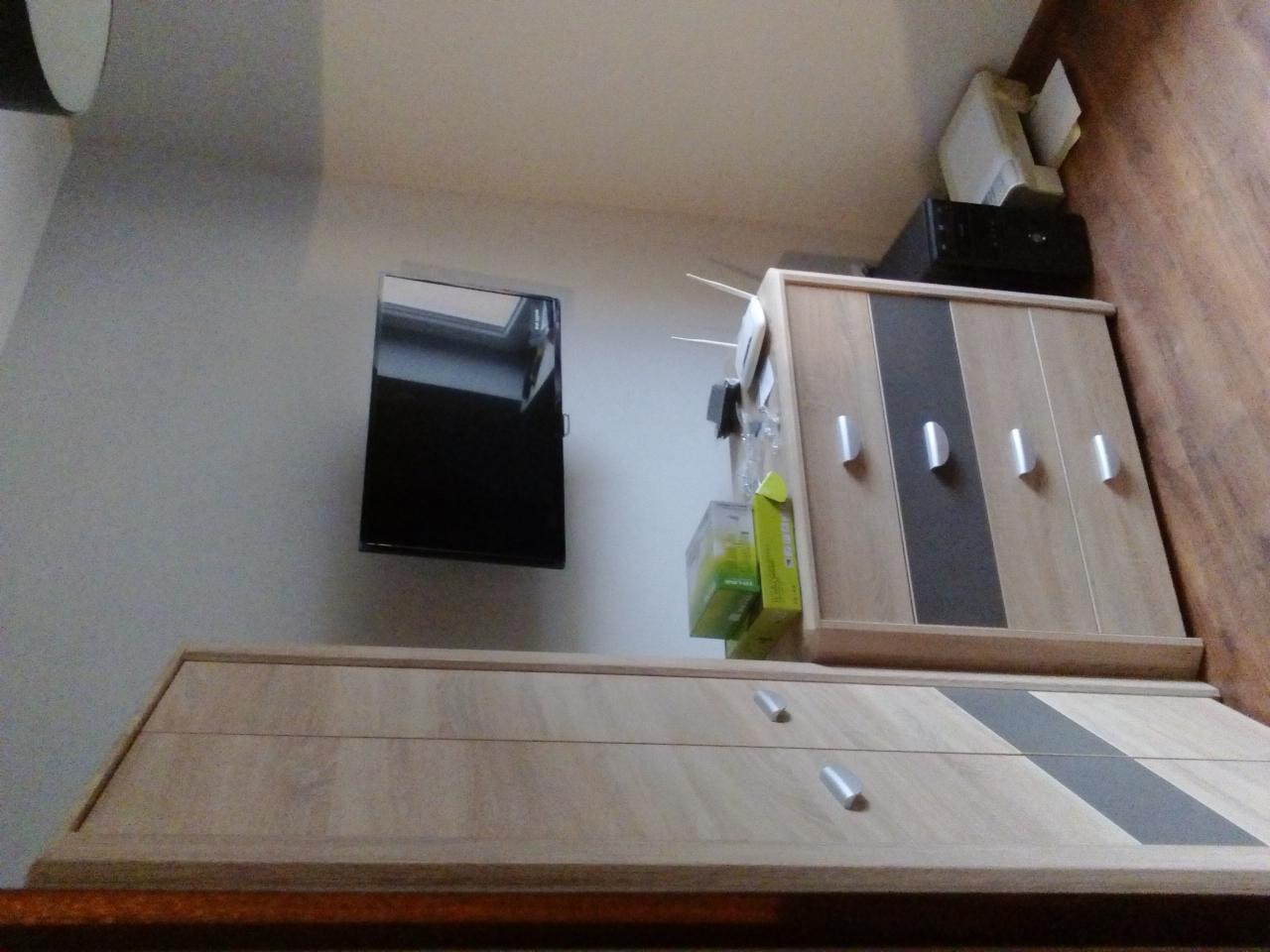 Ustawiona pod kątem komoda z szufladami i szafka wisząca z telewizorem na ścianie, widoczne akcesoria na szafce, drukarka i router.