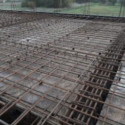 Siatka zbrojeniowa ułożona na szalunku, przygotowana do zalania betonem, widoczne plastikowe dystanse i wystające pręty.