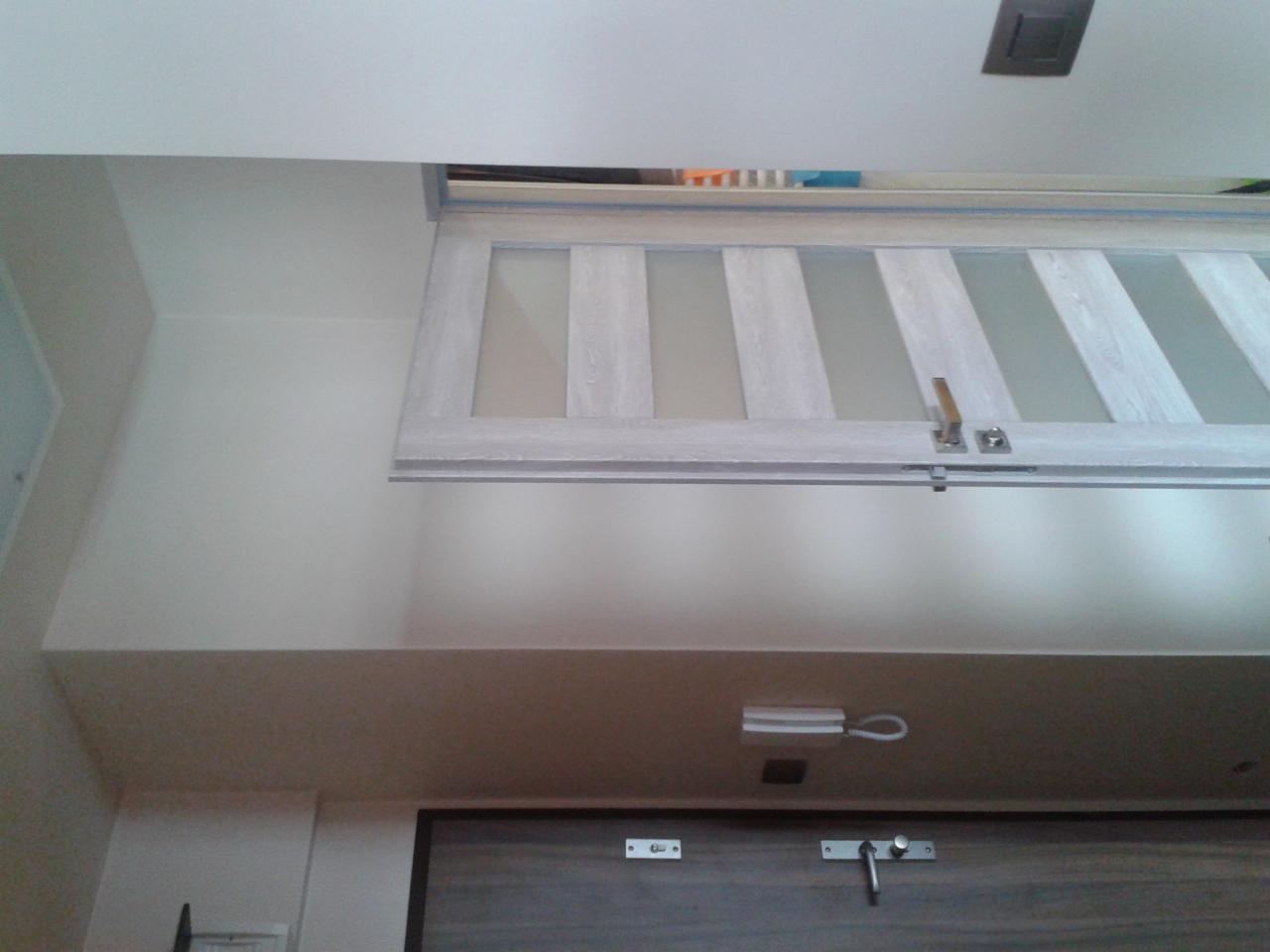 Szklane drzwi przesuwne w jasnej ramie, zamontowane pod sufitem, widoczne z dołu. Elementy wykończenia wnętrza.