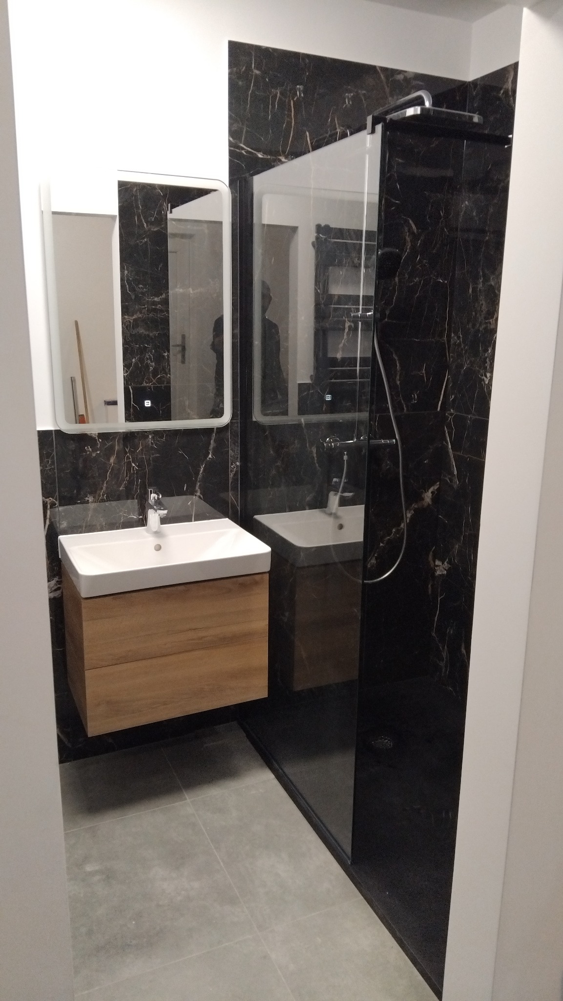 Nowoczesna łazienka w Kątnie z czarnymi marmurowymi płytkami, drewnianą szafką pod umywalką i szklaną kabiną prysznicową. Minimalistyczny design.