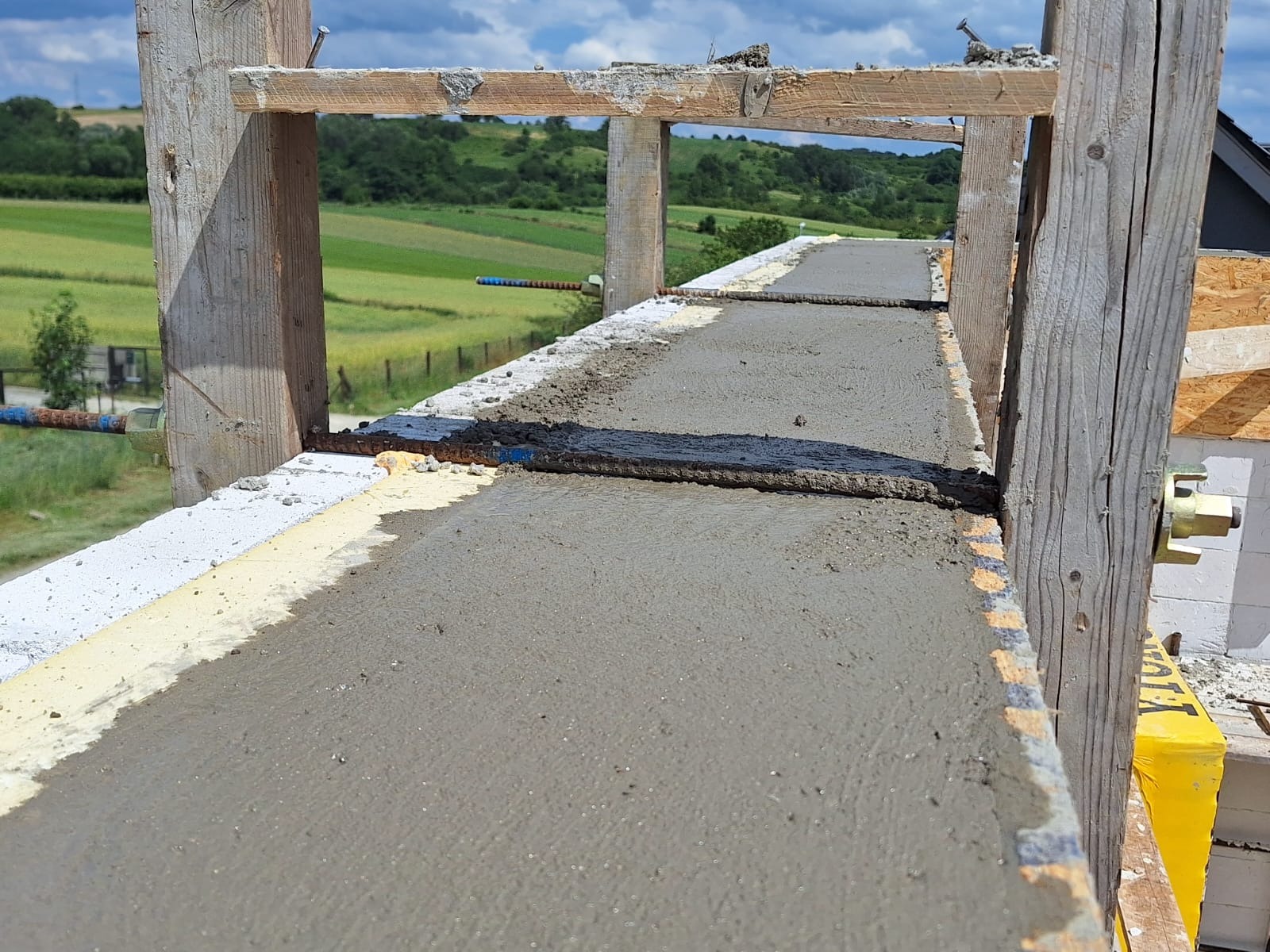 Wylewanie betonu na szalunek z widocznym zbrojeniem i elementami drewnianymi konstrukcji, w tle zielony krajobraz