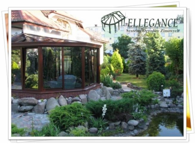 Szklana oranżeria z brązowymi ramami, przylegająca do domu, otoczona ogrodem skalnym i oczkiem wodnym. W tle widoczne drzewa i budynek.