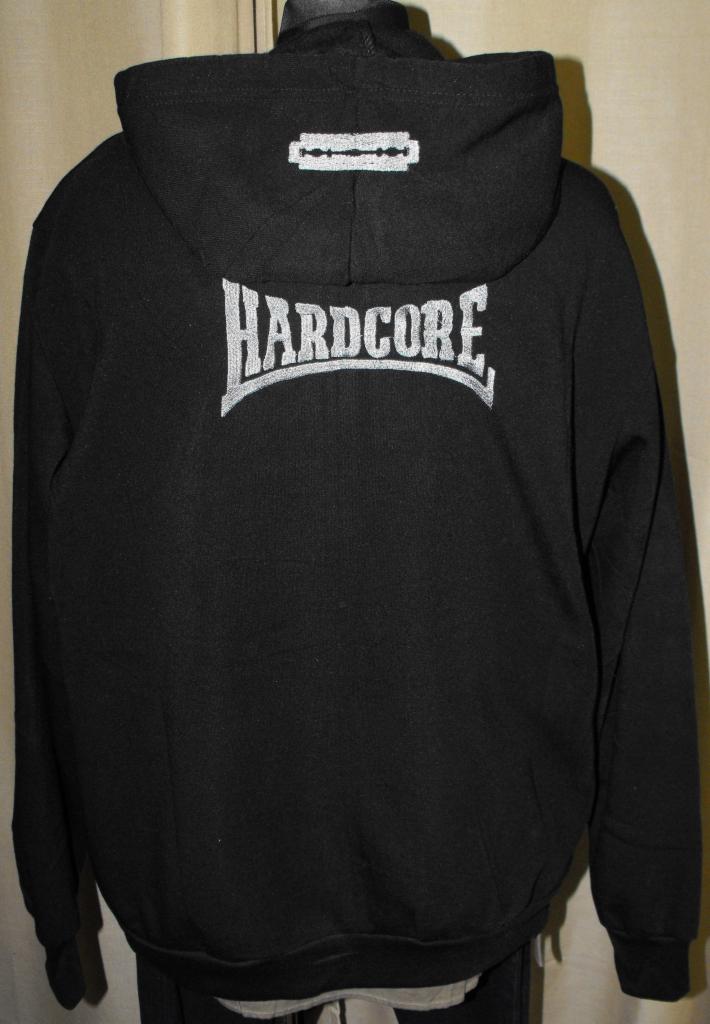 Czarna bluza z kapturem, na plecach srebrny napis 'HARDCORE' i grafika żyletki. Widok z tyłu, stonowane oświetlenie, ciemne tło.