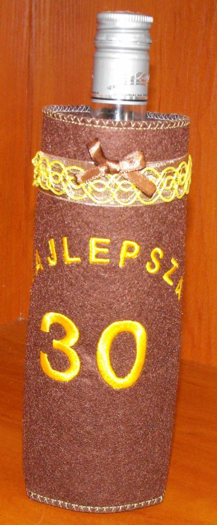 Ozdobna, brązowa osłonka na butelkę z żółtym napisem 'Najlepsza 30', wykończona wstążką i haftem, idealna na prezent urodzinowy.