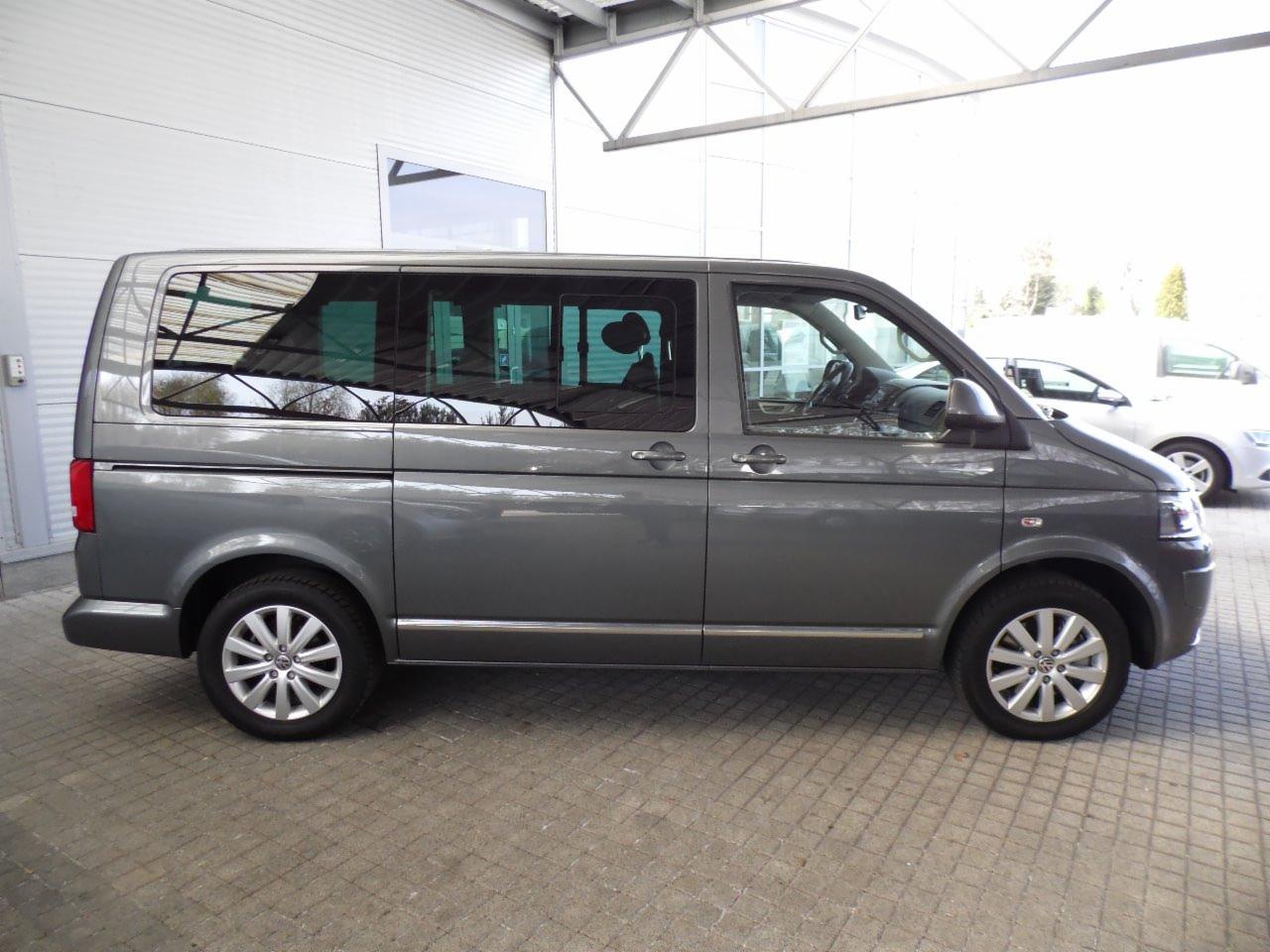 Szary van Volkswagen Transporter T5, widok z boku na tle hali z oknami, z chromowanymi listwami i aluminiowymi felgami.