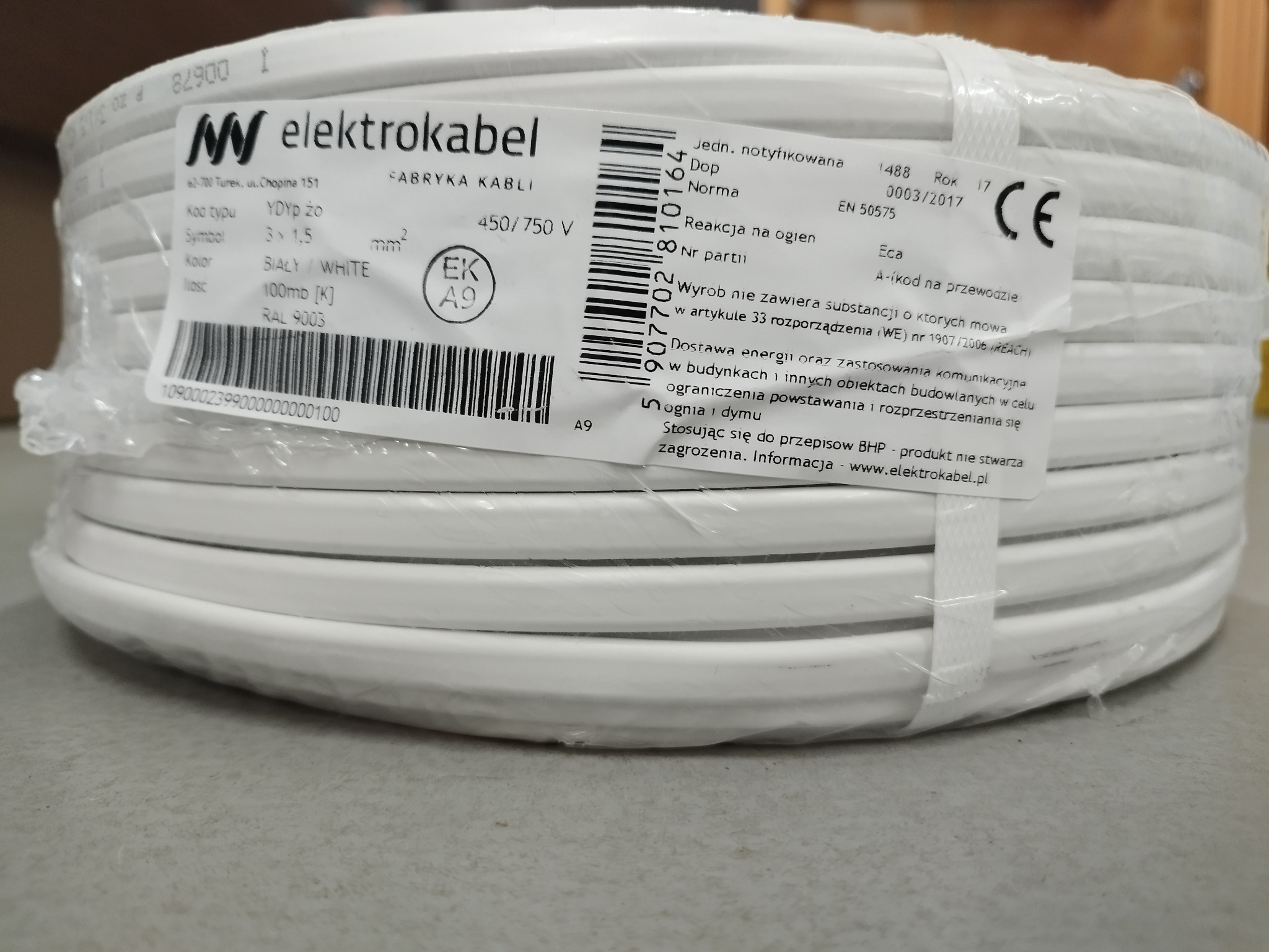 Zwój białego kabla elektrycznego YDYp Żo 3x1,5mm² w przezroczystej folii, etykieta producenta Elektrokabel z informacjami technicznymi i certyfikatami.