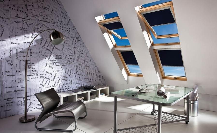 Poddasze z trzema oknami dachowymi wyposażonymi w zaciemniające rolety wewnętrzne, widok na błękitne niebo, na ścianie tapeta w mapę miasta, nowoczesny fotel i szklany stolik na kółkach.