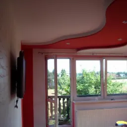 Stylowy salon z dekoracyjnym, czerwonym sufitem podwieszanym, widokiem na zieleń przez okno i telewizorem na ścianie z efektem dekoracyjnym.