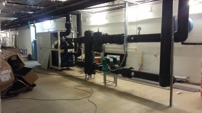 Rozbudowana instalacja przemysłowa z rurami, zaworami i pompami, z widocznym agregatem chłodniczym w tle. Elementy izolacji termicznej na rurach.