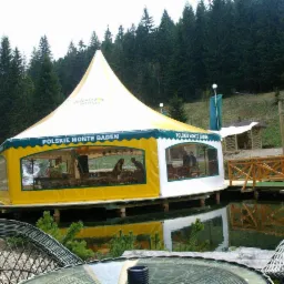 Namiot z napisem 'Polskie Monte Baden' ustawiony na platformie na wodzie, widok z zewnątrz, w tle las.