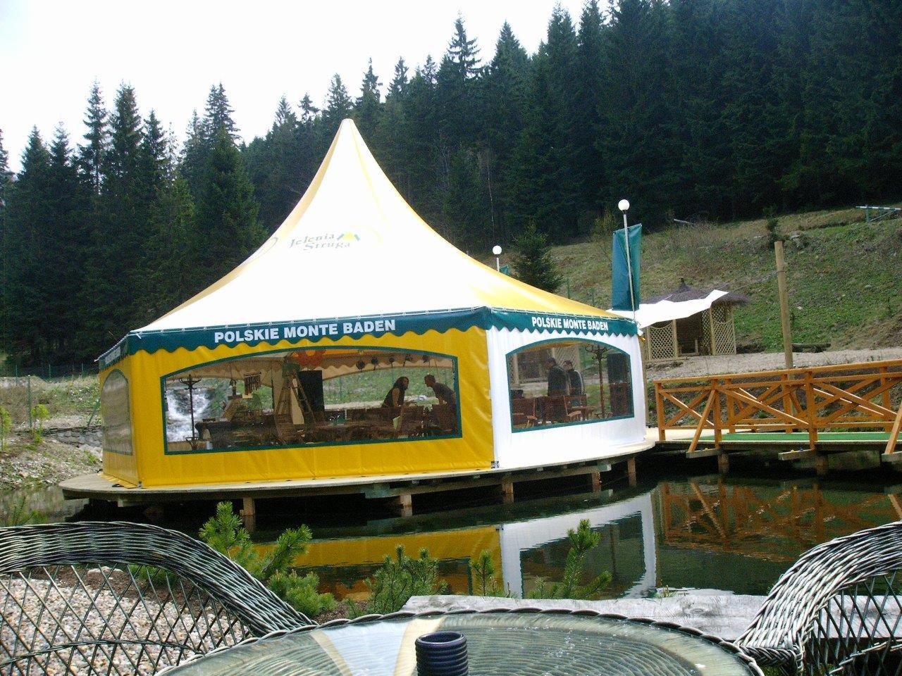 Namiot z napisem 'Polskie Monte Baden' ustawiony na platformie na wodzie, widok z zewnątrz, w tle las.
