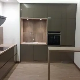 Nowoczesna kuchnia w odcieniach brązu i beżu, z zabudową kuchenną, płytą indukcyjną, piekarnikiem i drewnianą podłogą. Minimalistyczny design i funkcjonalność.