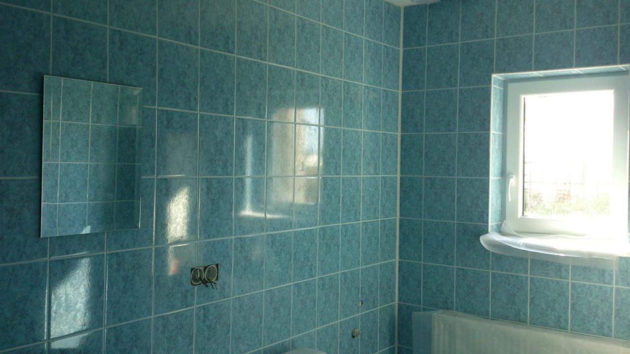 Wykończona łazienka z niebieskimi płytkami, lustrem na ścianie i oknem z widocznym światłem dziennym, zabezpieczonym parapetem.