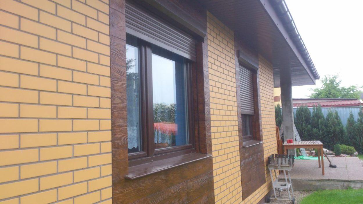 Elewacja budynku z żółtej cegły z brązowymi oknami z roletami zewnętrznymi i okładziną imitującą drewno.