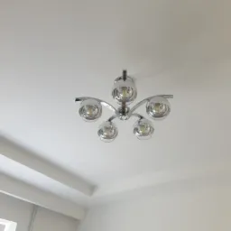 Chromowana lampa sufitowa z pięcioma szklanymi kloszami w kształcie kuli, zamontowana na białym suficie z dekoracyjnymi listwami.