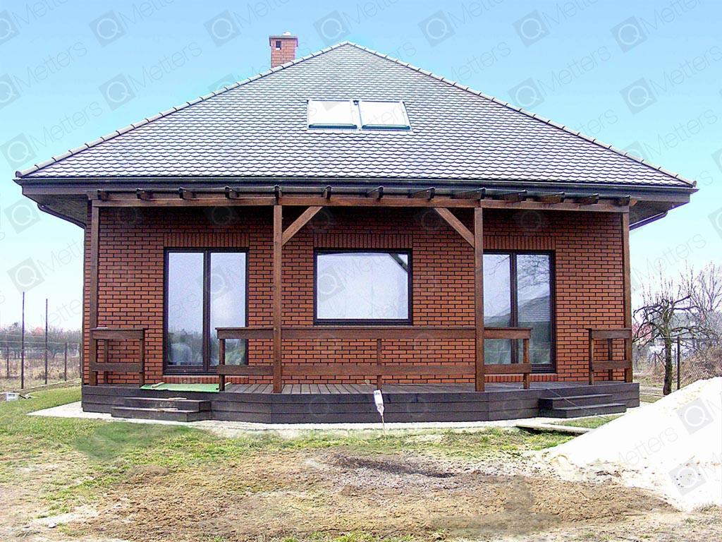 Parterowy dom z cegły klinkierowej z drewnianą werandą, dachówką ceramiczną i oknami z ciemną stolarką. Widok z zewnątrz na tle zieleni i częściowo ośnieżonego terenu.