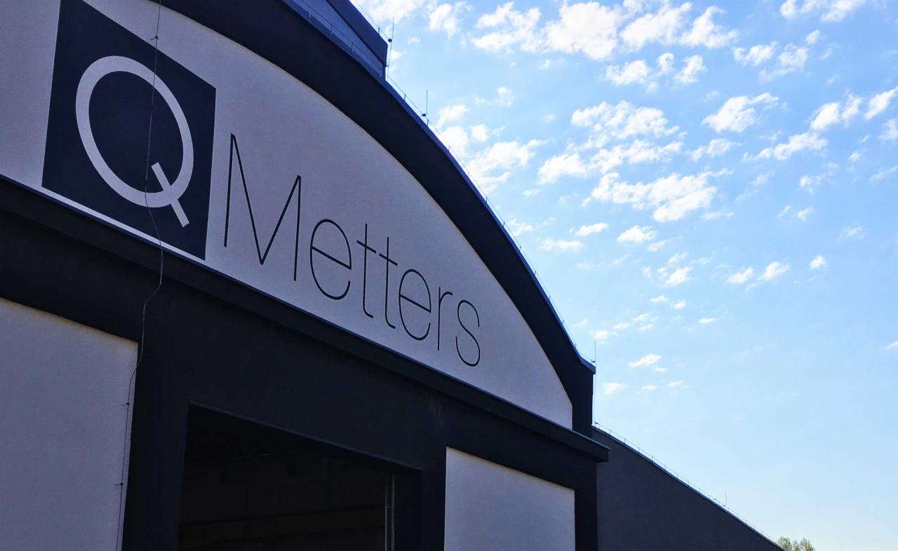 Elewacja budynku z logo firmy Metters na tle błękitnego nieba z chmurami.