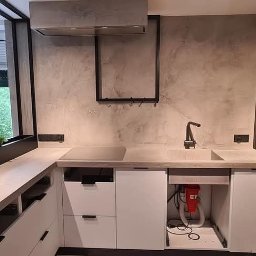 BB DESIGN - Nowoczesna kuchnia z szarą, teksturowaną ścianą, zabudową kuchenną w kolorach bieli i drewna, czarną armaturą i oknem z widokiem na zieleń.