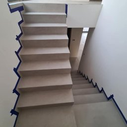 BB DESIGN - Betonowe schody wewnętrzne w trakcie budowy, zabezpieczone niebieską taśmą malarską, widok z góry na dół.